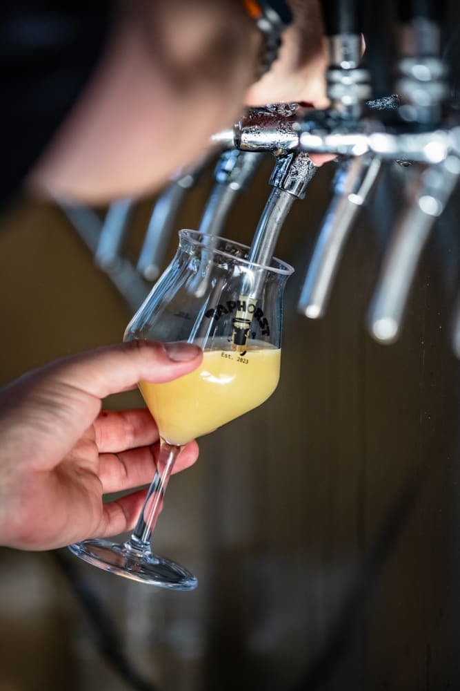 A glass of craft beer being poured at the tap wall