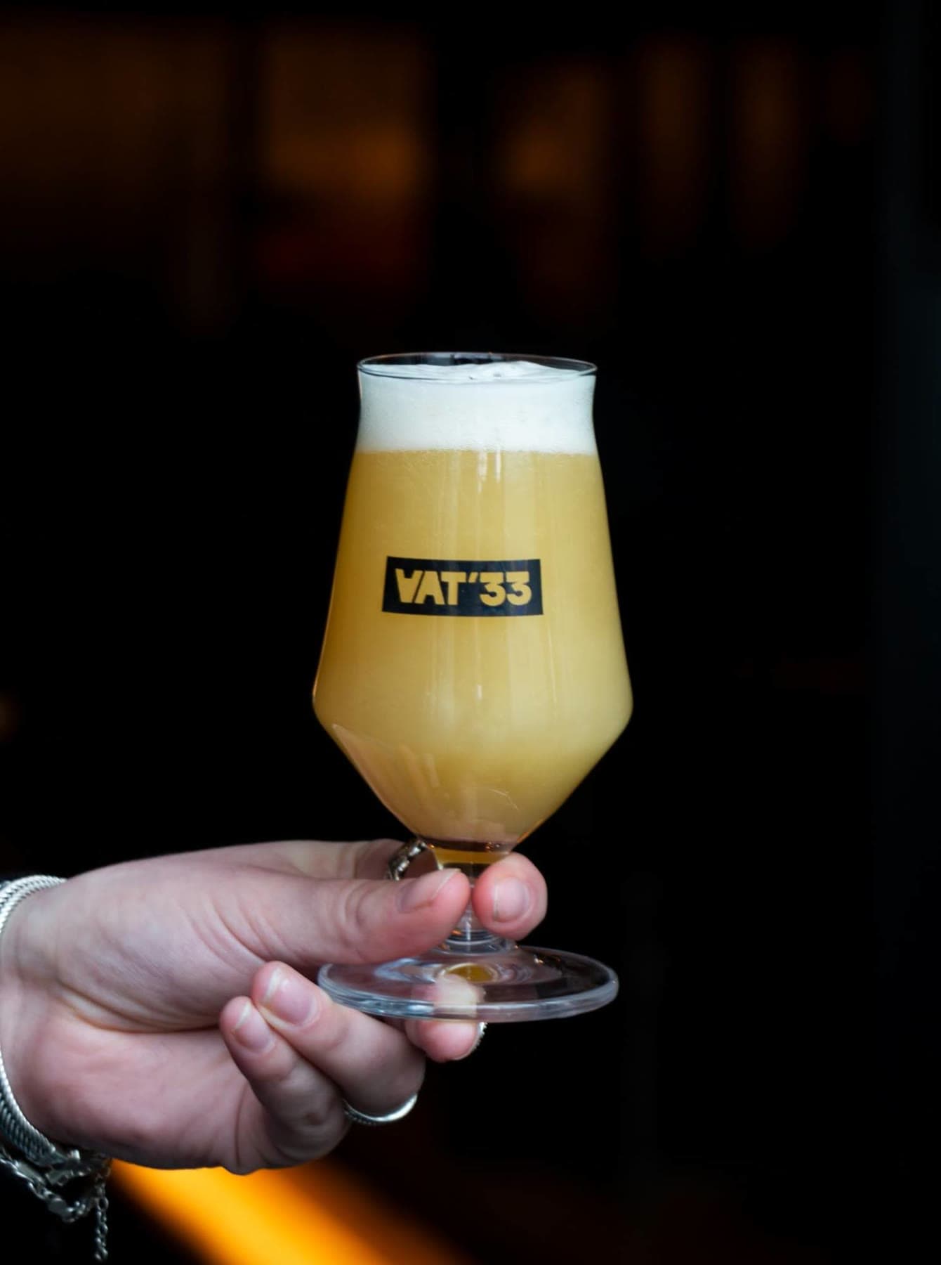 A VAT'33 glass of hazy beer, held up in one hand