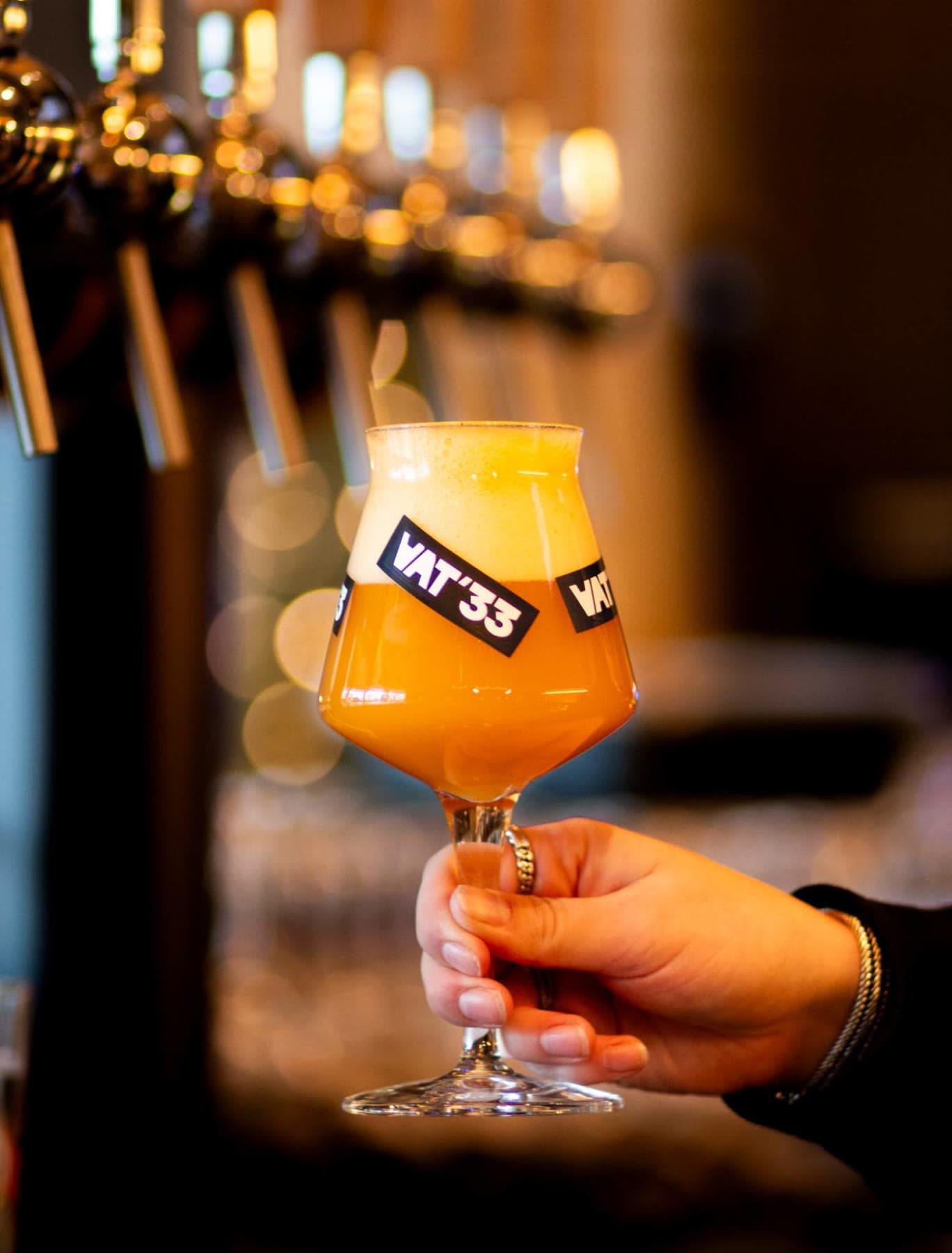 A VAT'33 glass of hazy IPA in front of the Tjaps tap wall