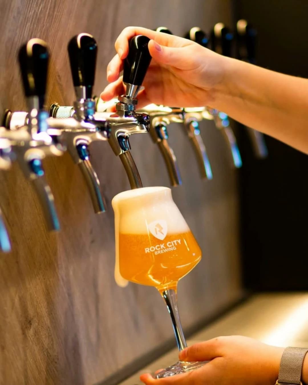 A tulip glass being filled at the tap wall; the foam runs over the rim