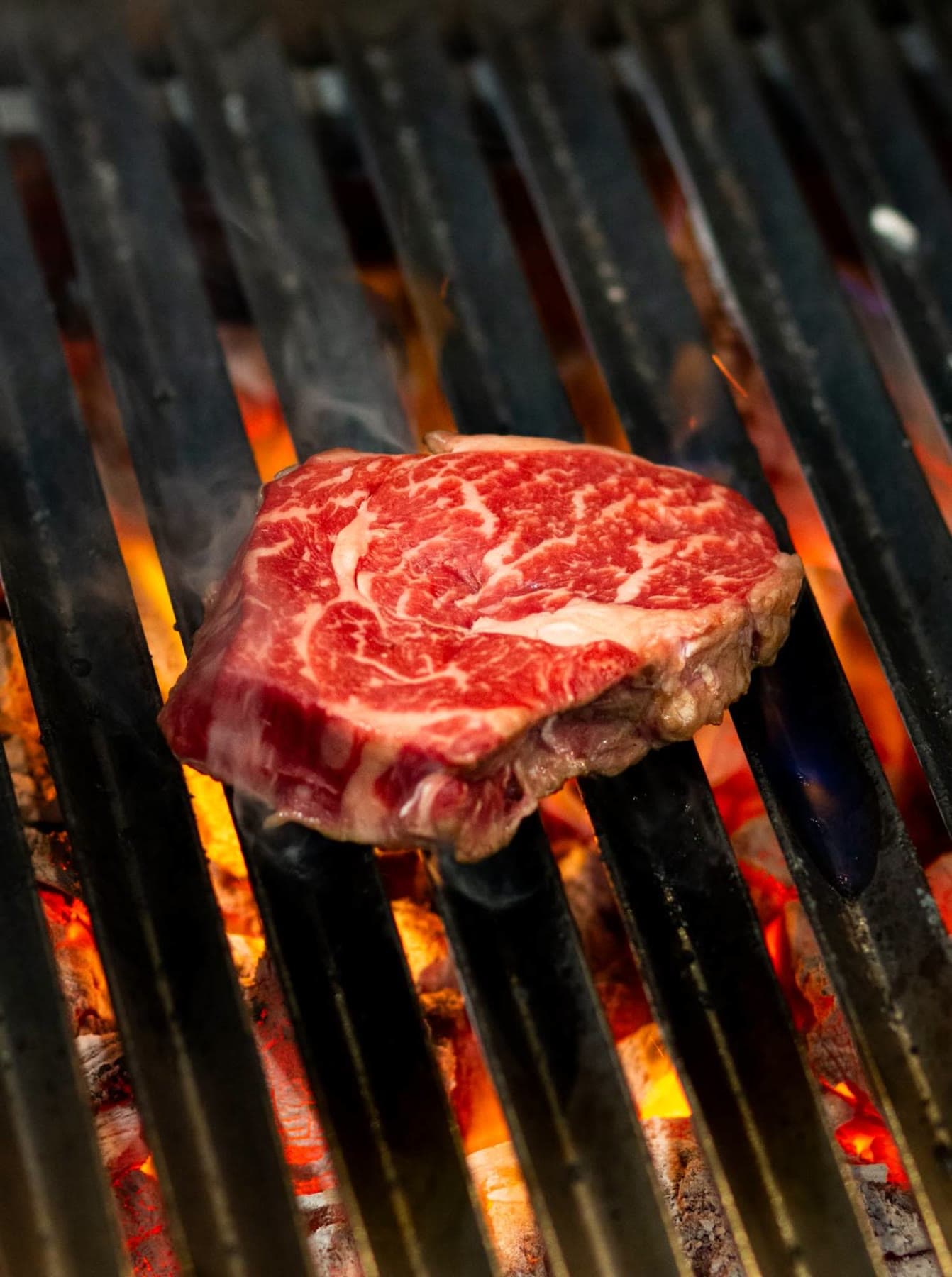 A raw rib-eye above glowing coals