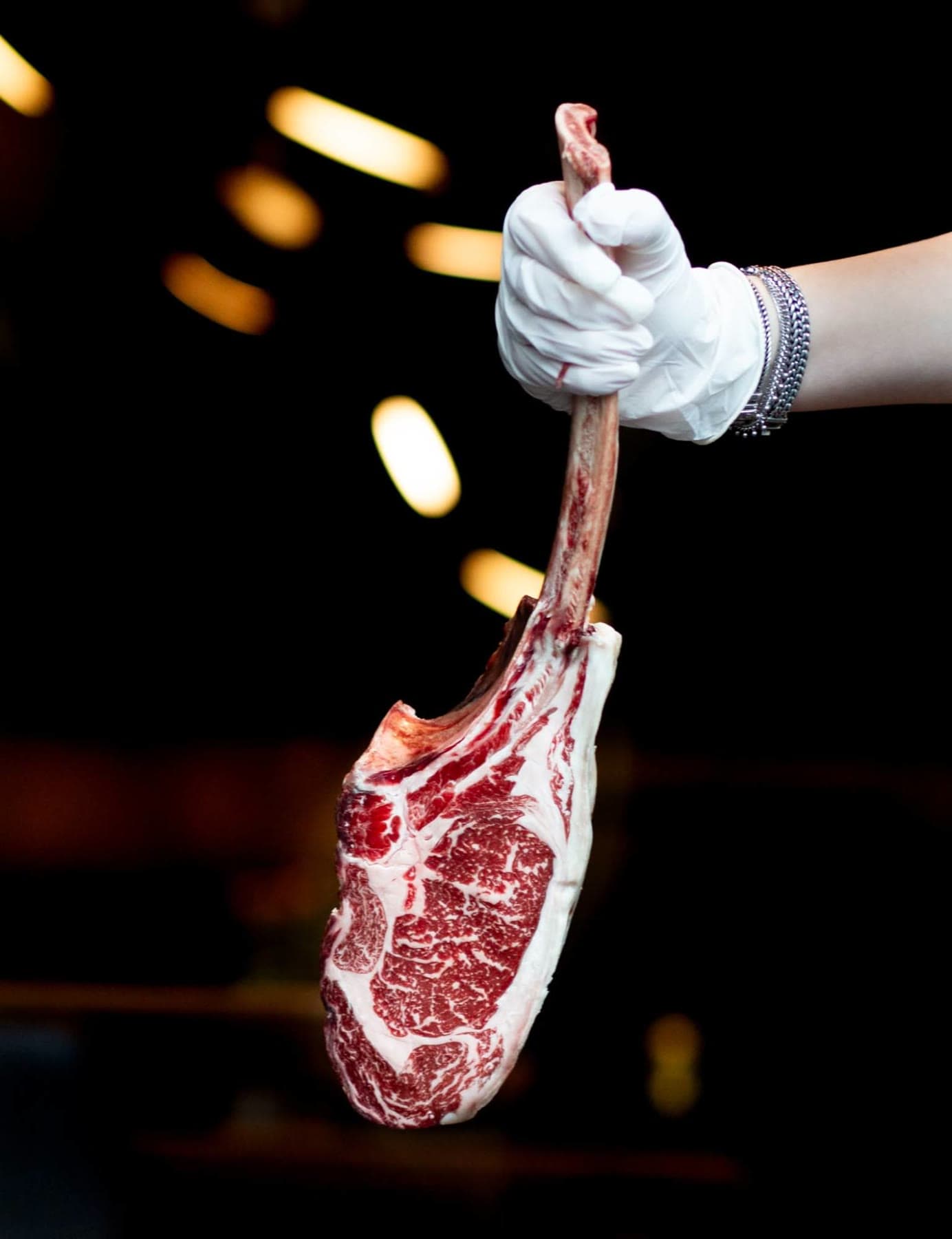 A raw tomahawk from a dual-purpose cow on the bone, held in a white glove
